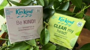 KinKind Be Kind and Clear My Head shampoo bars photographed among green leaves in natural light, showing their plastic-free packaging.