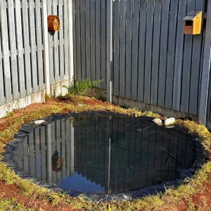 Completed DIY natural pond filled with water, surrounded by a grey wooden fence and rocks