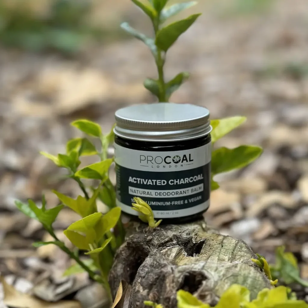 Procoal Activated Charcoal Natural Deodorants Balm in a jar, placed outdoors on a log surrounded by green leaves.