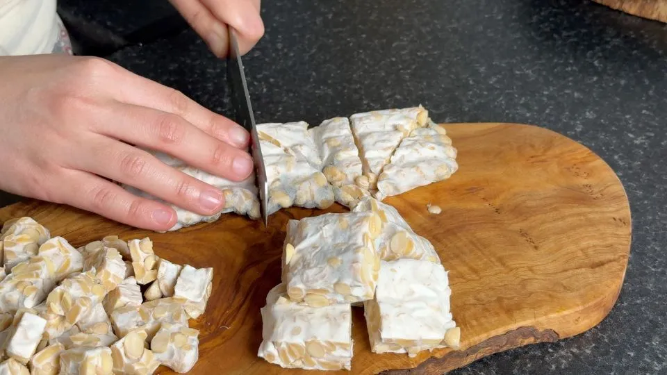 chopping tempeh on wooden chopping board