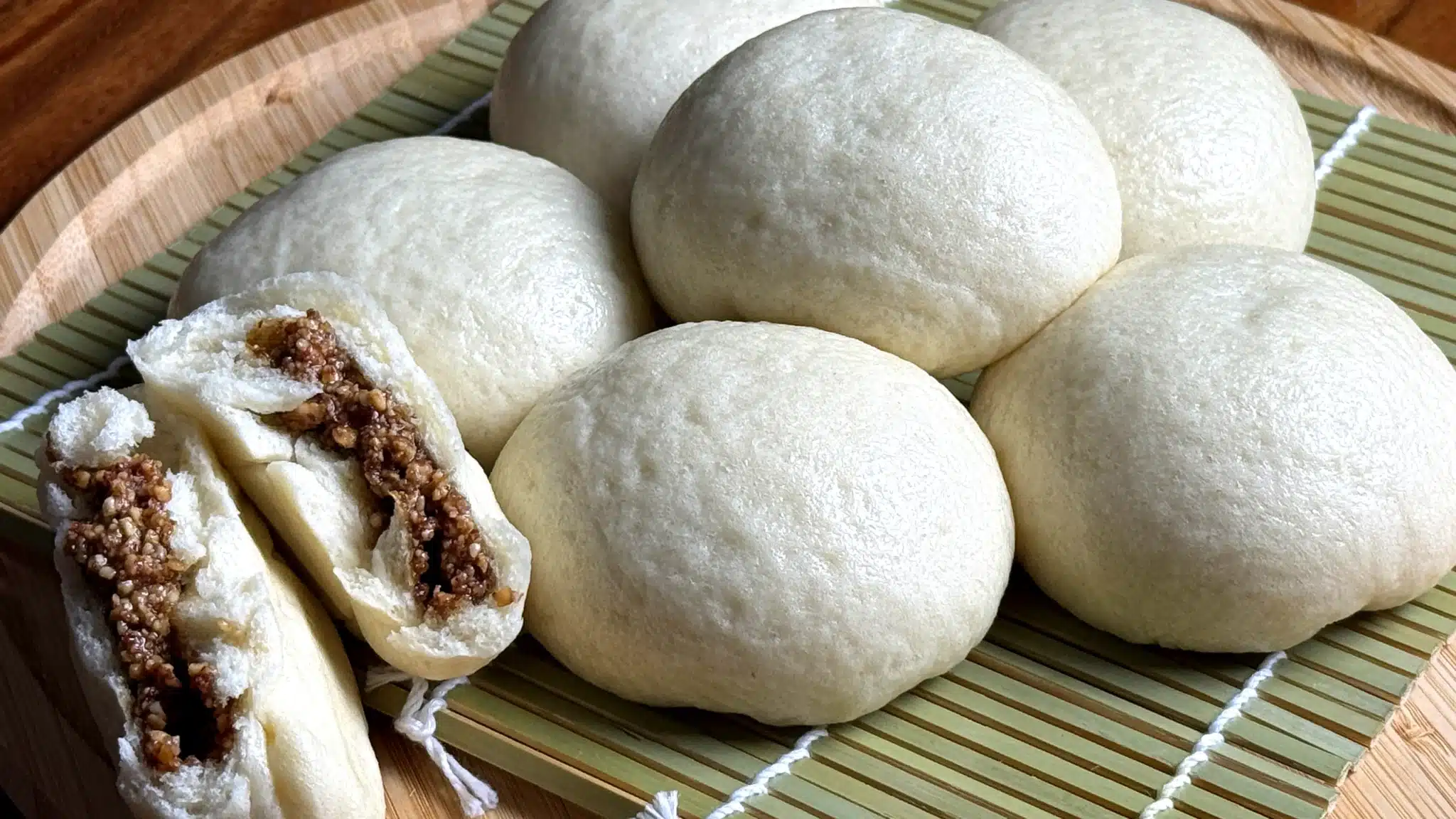 Peanut steamed buns on a bamboo mat, one split open to reveal a sweet crushed peanut and sesame filling